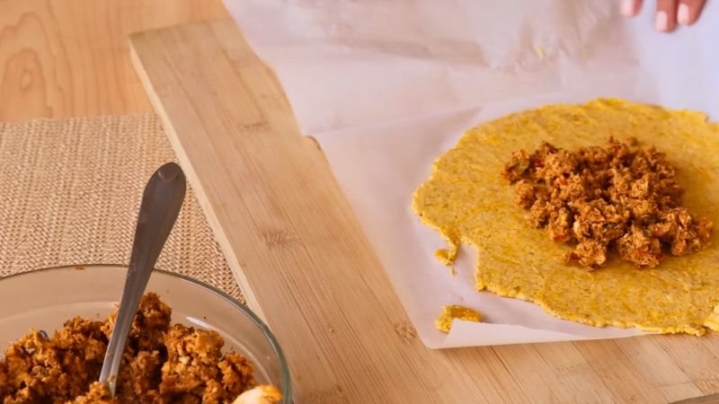 Colocando una cucharada de relleno de pollo sazonado sobre un círculo de masa de auyama extendido en papel encerado.