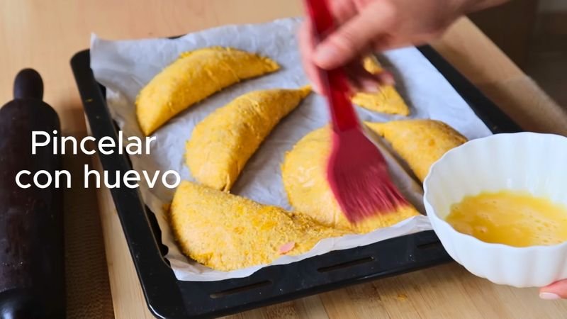 Pincelando empanadas de masa de auyama con huevo batido en una bandeja de horno antes de hornear.