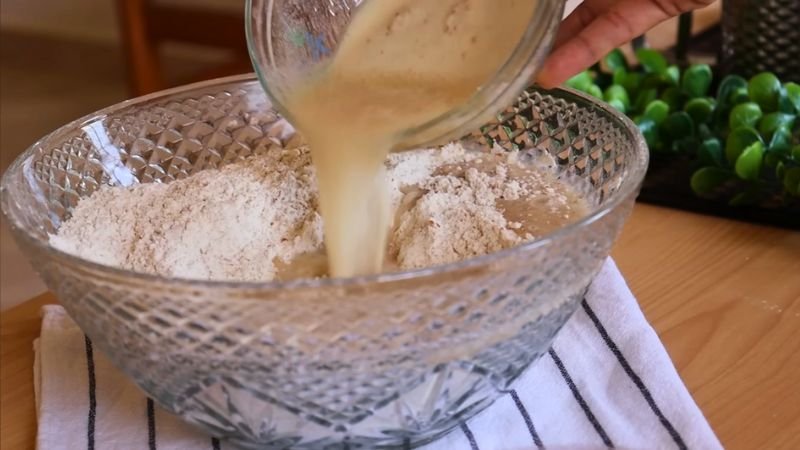 Mezcla de ingredientes Agregando la mezcla de levadura activada a la harina integral en un bol de vidrio para hacer pan casero
