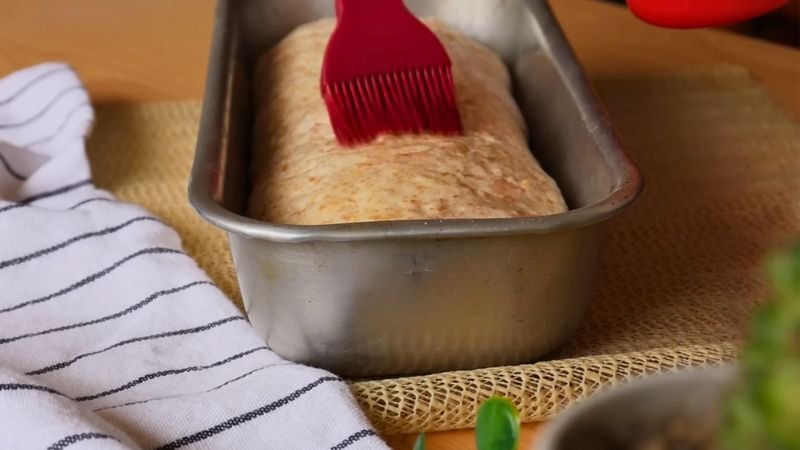 Masa lista para hornear en molde Pincelando masa de pan en un molde antes de hornear