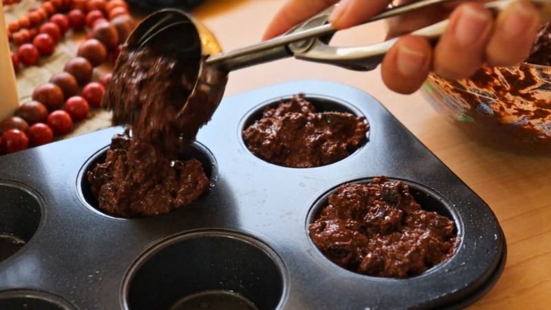 llenado-moldes-cupcakes-saludables-avena.jpg Llenando moldes para cupcakes saludables de avena y chocolate con una cuchara de helado.