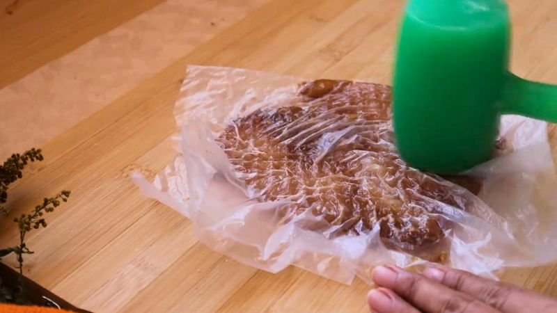 Ablandar pechuga de pollo - Coffee María Usando un mazo de cocina verde para ablandar filetes de pechuga para enrollado de pollo relleno bajo papel film.