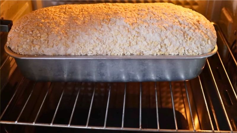 horneado-pan-integral-masa-madre-coffee-maria Pan integral de molde con cobertura de avena horneándose sobre la rejilla del horno, mostrando un crecimiento uniforme y dorado.