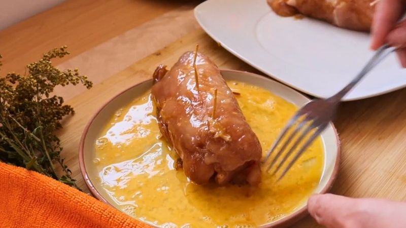 Pasar por huevo el pollo - Coffee María Sumergiendo un enrollado de pollo relleno en un cuenco con huevo batido para el proceso de empanizado.
