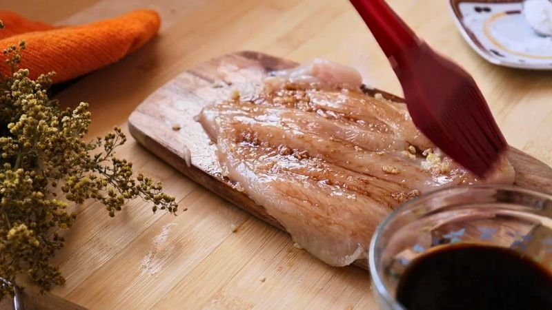 Sazonar filetes de pollo - Coffee María Sazonando filetes de pechuga con una brocha roja para preparar un enrollado de pollo relleno con ajo y salsa de soya.
