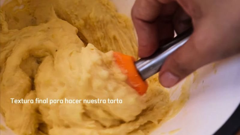 Textura final de la masa de papa - Coffee María. Mezcla de puré de papa con huevo y maicena siendo integrada con una espátula naranja para formar la base de la tarta.