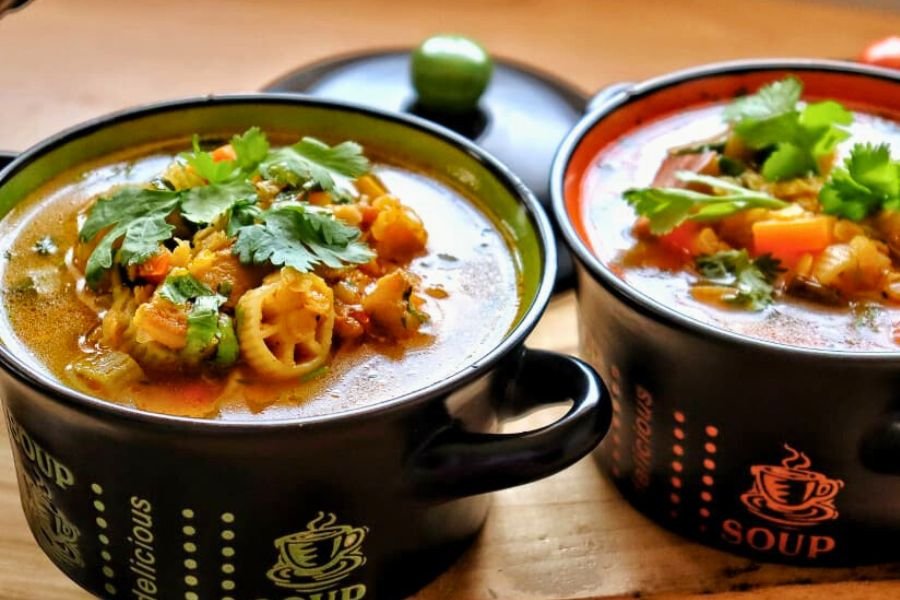Comidas Saludables Plato hondo con sopa de lentejas rojas con pasta de colores, trozos de chuleta y cilantro fresco, receta saludable de Coffee María.