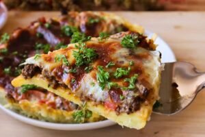 Porción de tarta de papa y carne molida con queso gratinado y perejil fresco en un plato blanco.