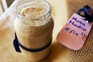 Masa madre desde cero activa en frasco de vidrio con etiqueta "Masa Madre Al Fin" y cinta azul, lista para hornear.