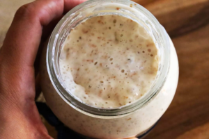 Primer plano del fermento de masa madre desde cero activa en un frasco de vidrio, mostrando burbujas y textura funcional.