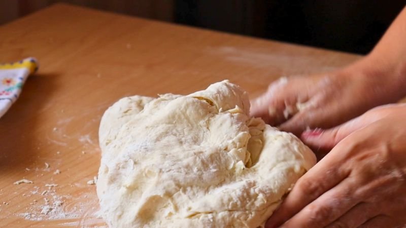 Manos trabajando la masa de pan francés sobre una superficie de madera tras la integración de ingredientes.