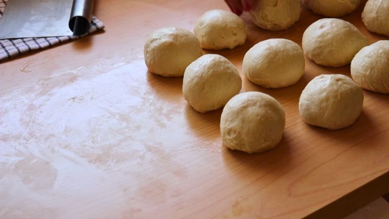Varias porciones de masa de pan francés perfectamente boleadas y organizadas sobre un mesón de madera.