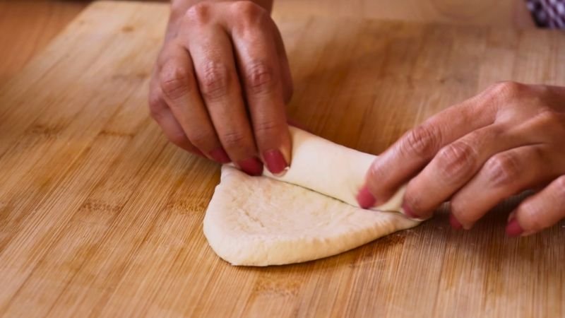 Manos enrollando una porción de masa sobre una tabla de madera para darle la forma alargada clásica del pan francés.