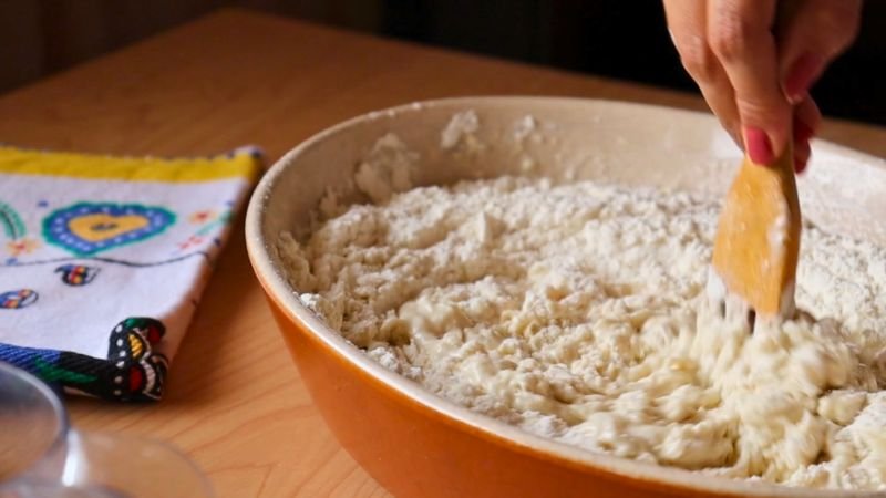 Mezcla manual de harina panadera, masa madre y agua fría en un bol para iniciar la masa.