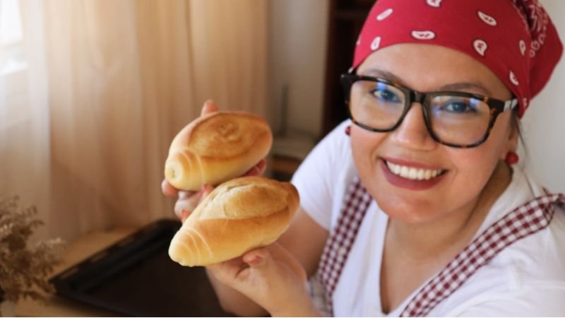 Maria de Coffee Maria MG sonriendo y sosteniendo dos panes franceses crujientes recién horneados.