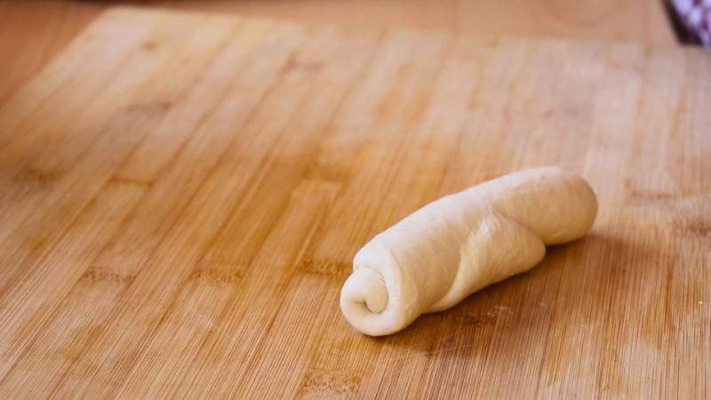 Una porción de masa de pan francés ya enrollada en forma de cilindro descansando sobre un mesón de madera.