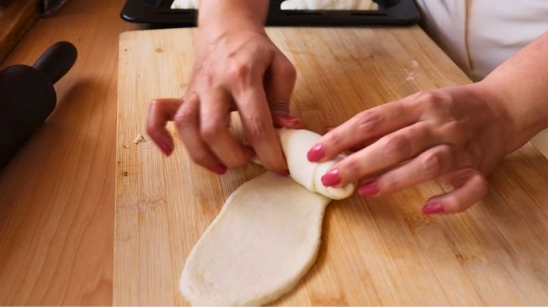 Detalle de las manos enrollando una porción de masa estirada sobre una tabla de madera para crear tensión.