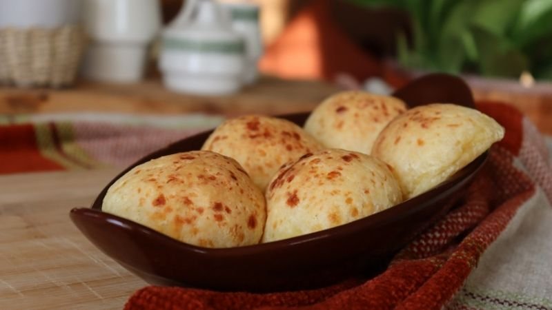 Fuente con varios pães de queijo tradicionales recién horneados, dorados y esponjosos.