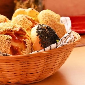 Canasta de mimbre con panes artesanales recién horneados, incluyendo panes con semillas y rellenos, sobre una mesa de madera en Coffee Maria.